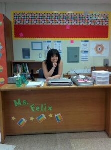 Natalie sitting in her classroom with her elbow under her chin, smiling. 